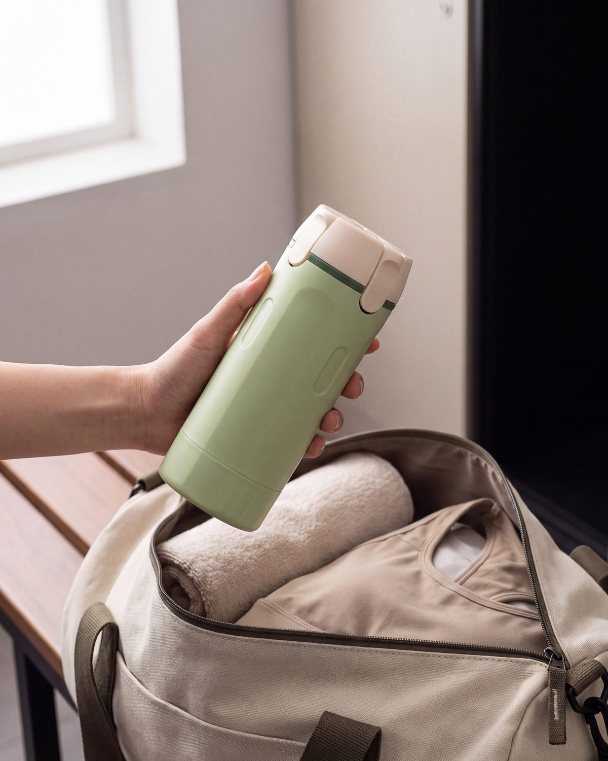 Hand lifting the Lathrio 4-in-1 travel dispenser out of a gym bag on a locker room bench