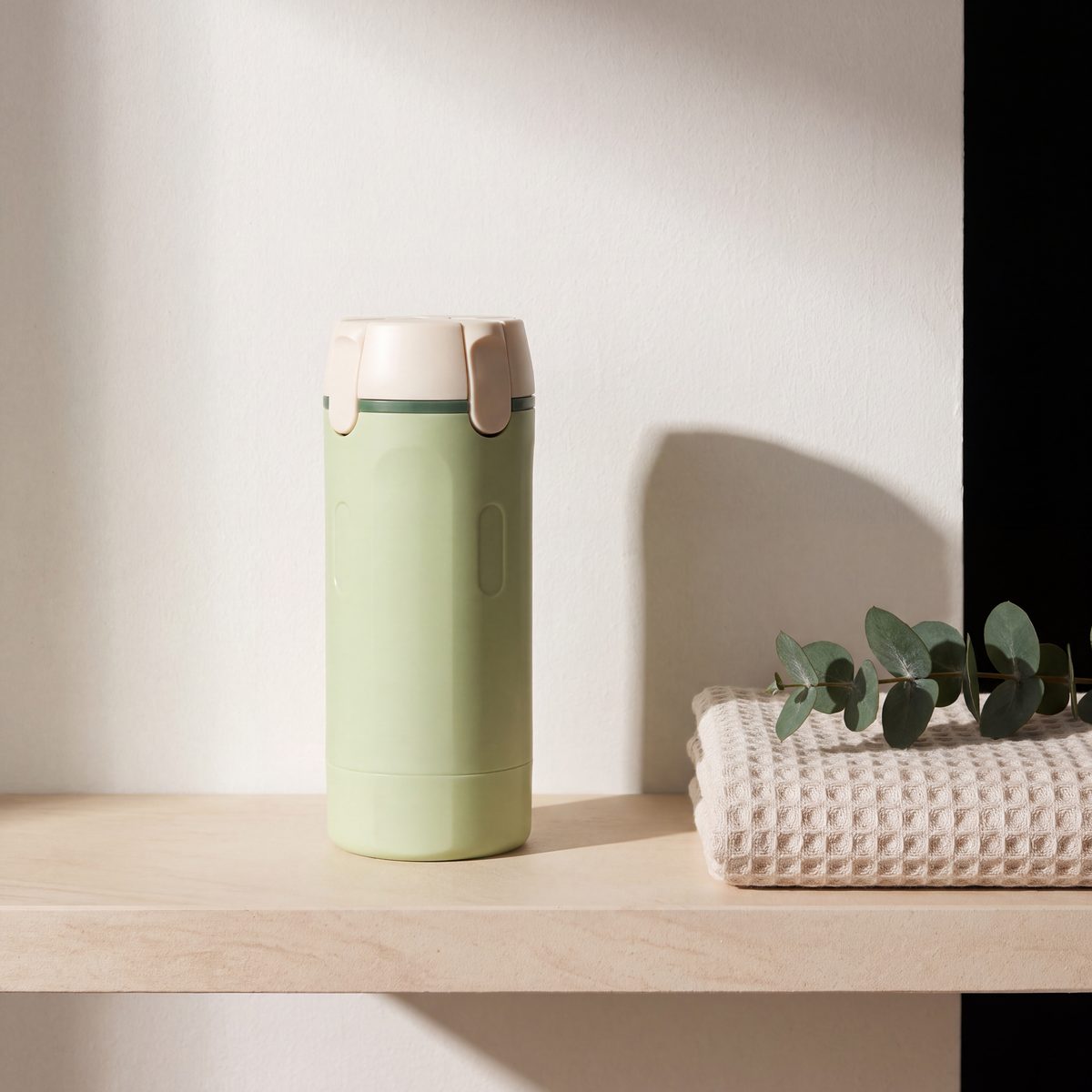 Lathrio travel dispenser standing on a bathroom shelf beside a folded towel