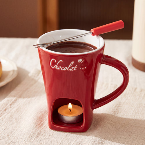 Taza fondue de chocolate roja con vela encendida en la base
